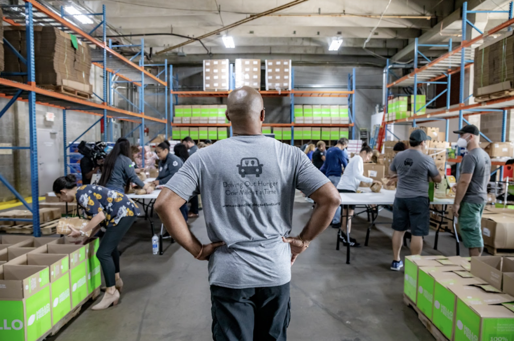 Man overseeing individuals prepping Meals with Meaning Food boxes in a warehouse